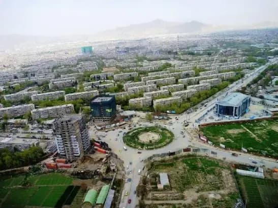 An aerial view of Kabul, tree-lined blocks with mountains behind