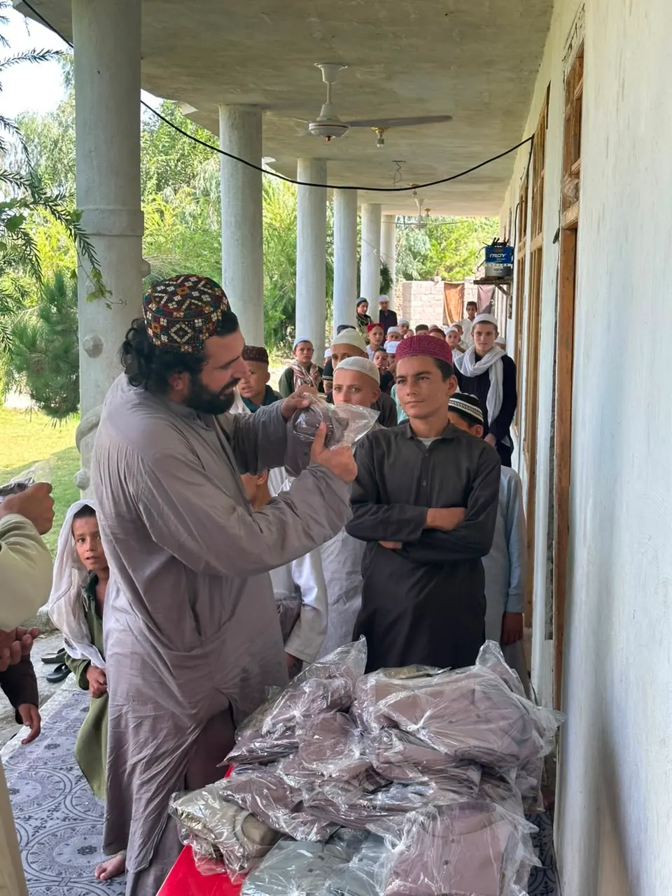 Abdulrahman Chonish handing packaged clothes to boys lined up on a veranda