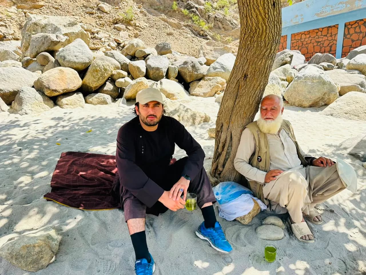 Abdulrahman Chonish and an elder drinking green tea under a tree on river sand