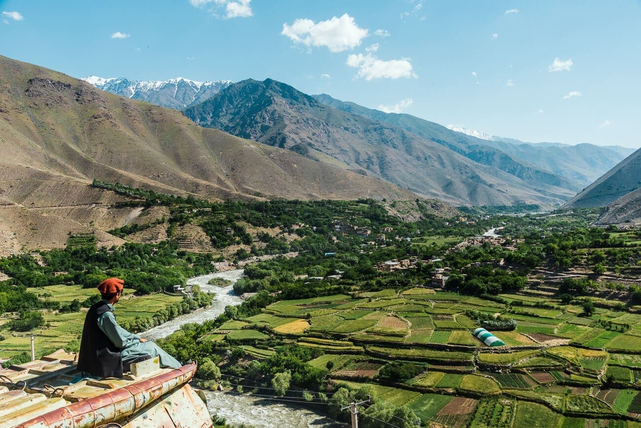 A man in a pakol overlooking a terraced river valley