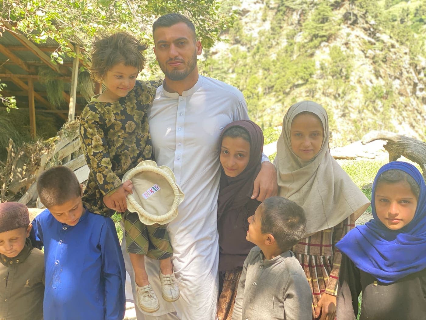 A young man holding a toddler, surrounded by village children