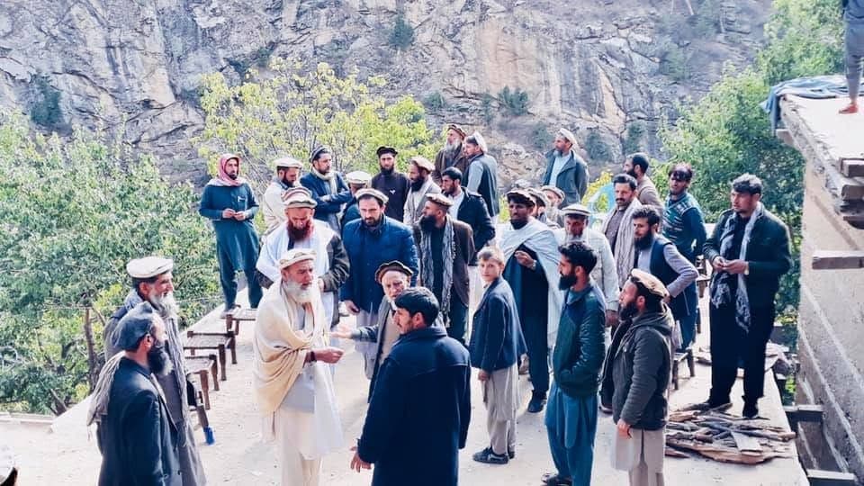 A large group of men talking on a terrace below a cliff