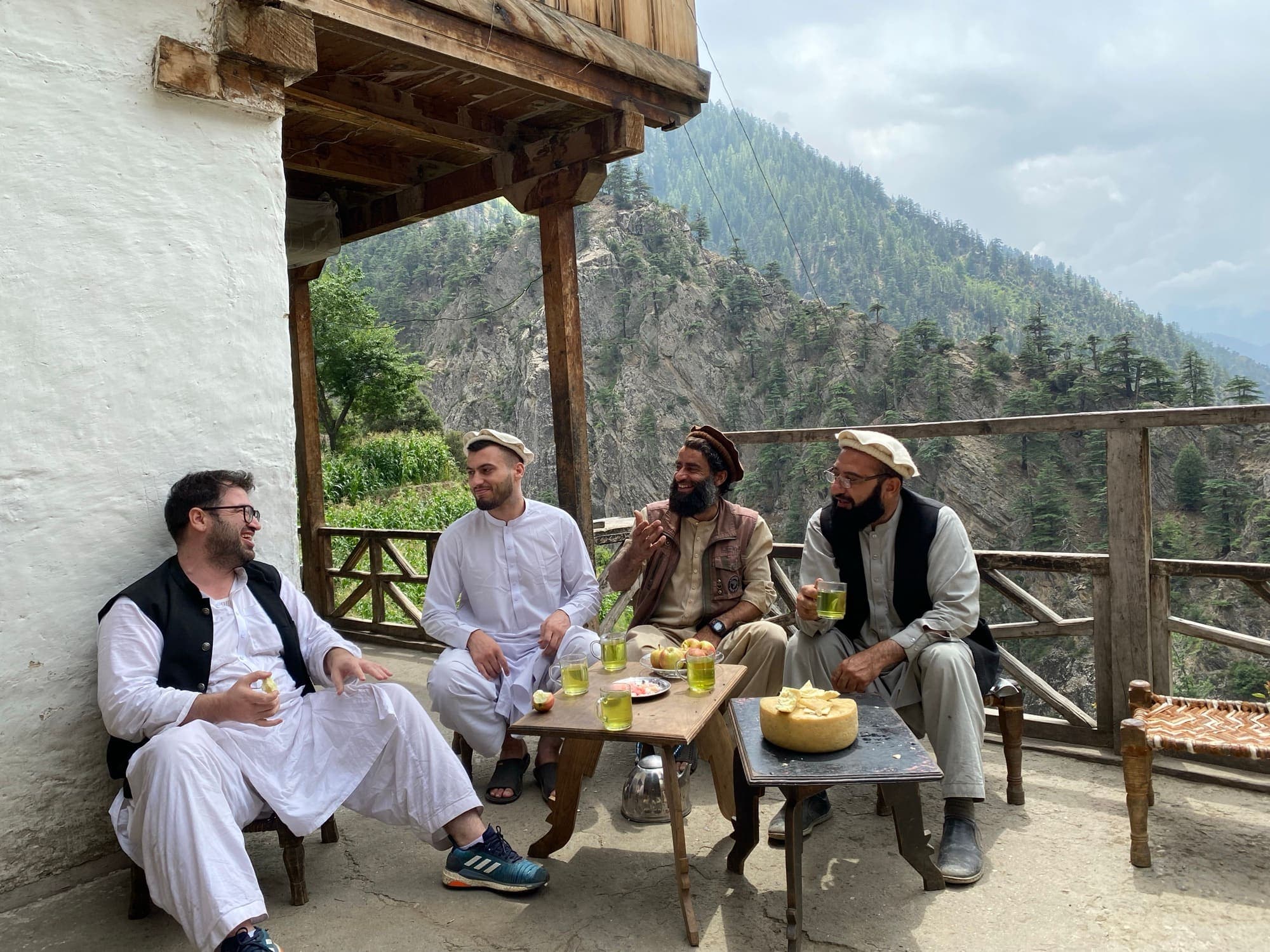 Four men sharing green tea, apples and local cheese on a carved wooden veranda