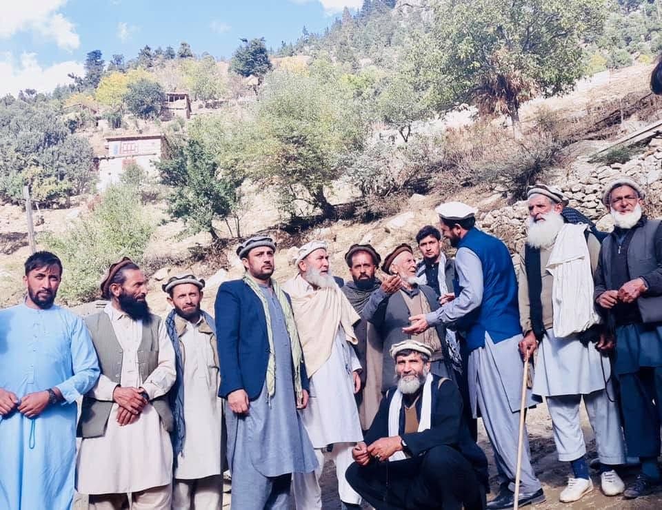 A group of village men in pakols and shawls posed on a hillside