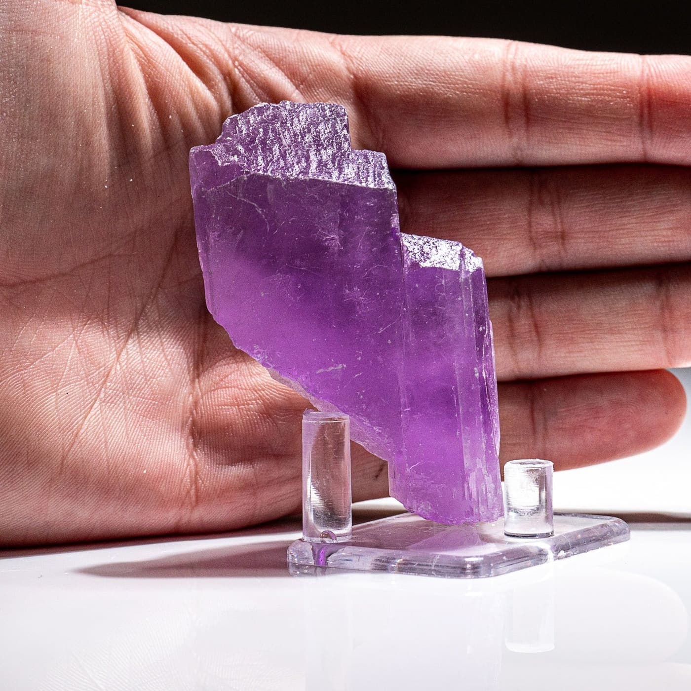 A lilac crystal displayed on a stand in front of an open hand
