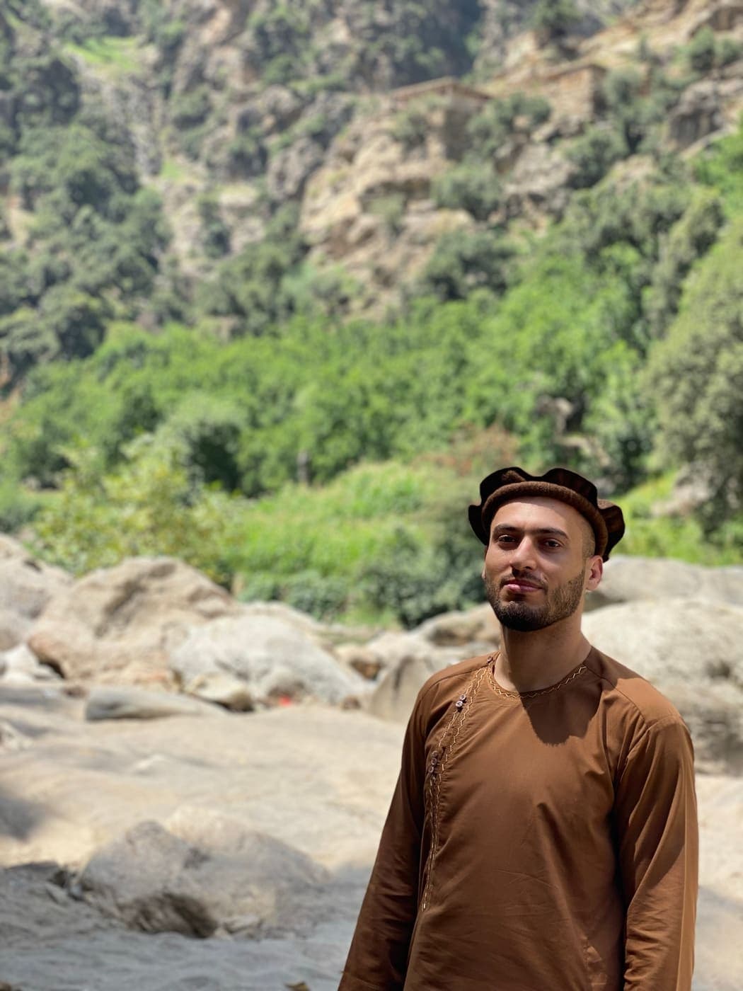 A man among river boulders in a deep gorge, village on the cliff above