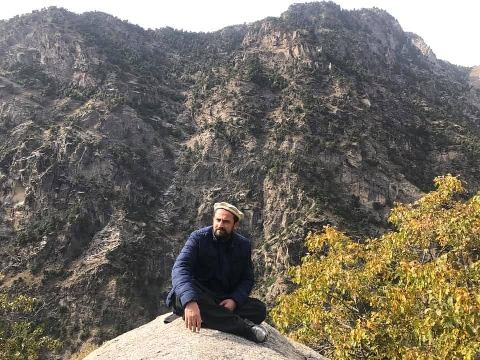 Obaid Nuristani seated on a boulder below a rock mountainside
