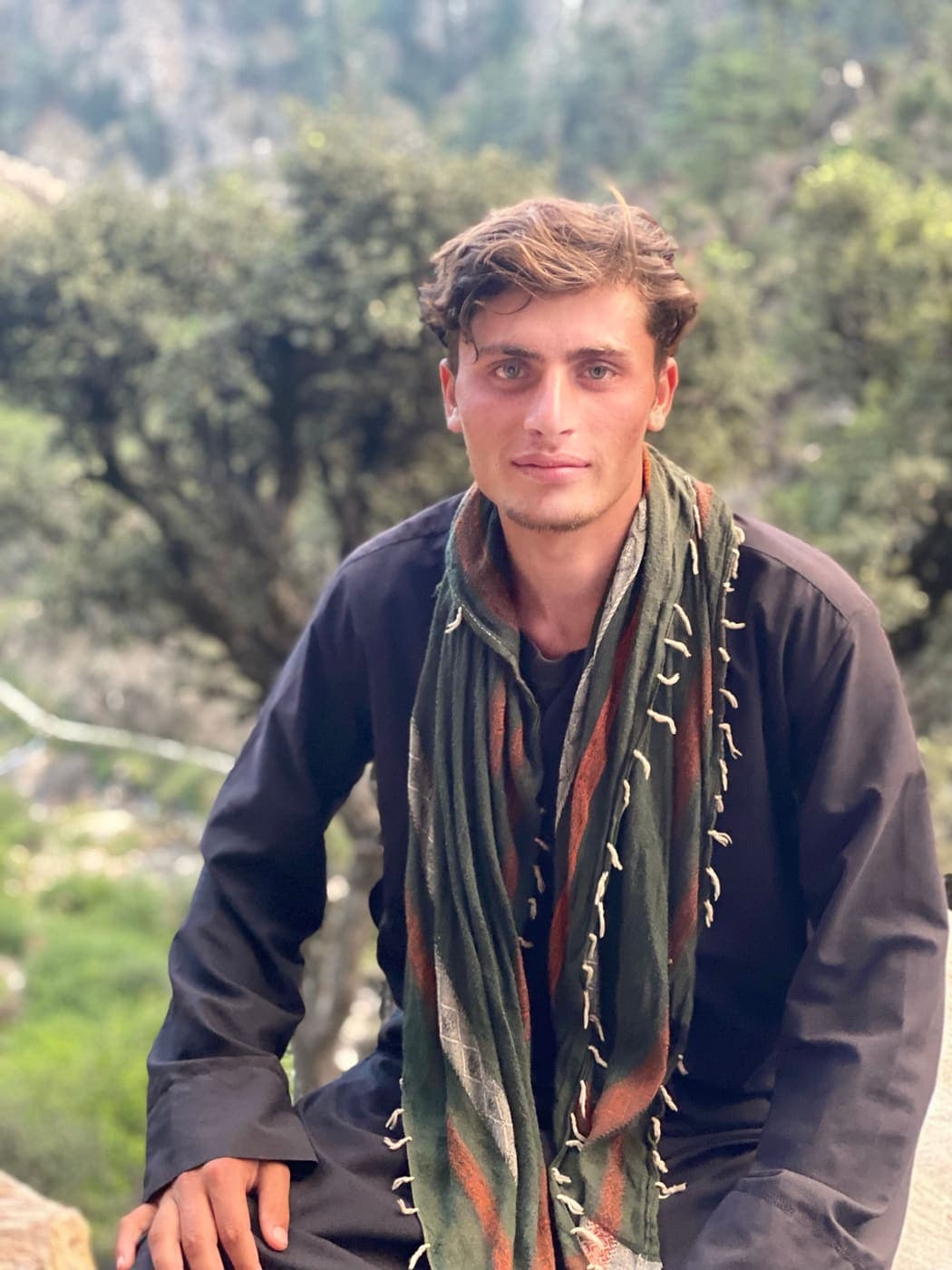 A young Nuristani man in a traditional scarf, the mountains behind him